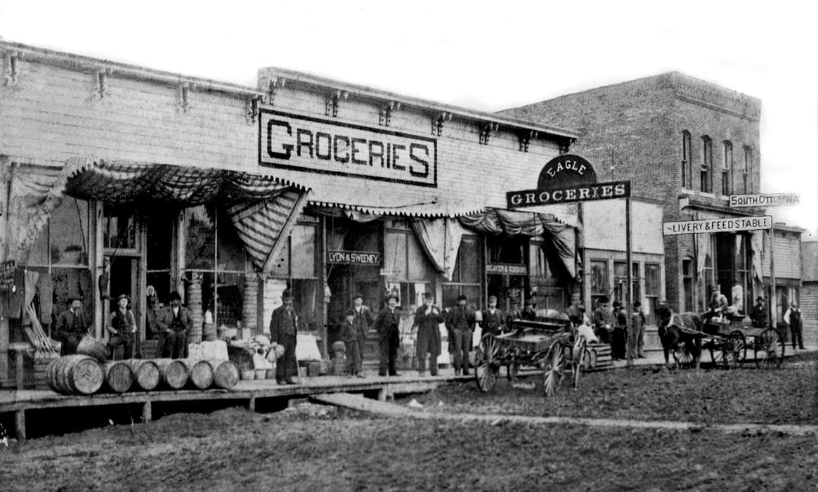 store, livery, history of Iowa, awning, Animals, barrel, wagon, Iowa History, Iowa, Main Streets & Town Squares, feed stable, Ottumwa, IA, Cities and Towns, Portraits - Group, Lemberger, LeAnn, Businesses and Factories, dirt road, horse, cart, grocery store
