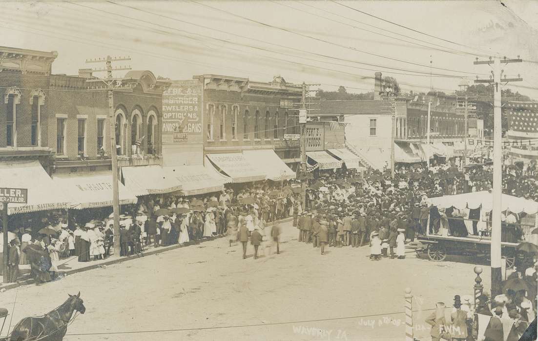 Fairs and Festivals, telephone line, e. bremer ave., Iowa History, celebration, gathering, parade, awning, dirt road, horse, Meyer, Mary, buildings, windows, wagon, crowd, Businesses and Factories, Iowa, history of Iowa, Main Streets & Town Squares, storefront, Cities and Towns