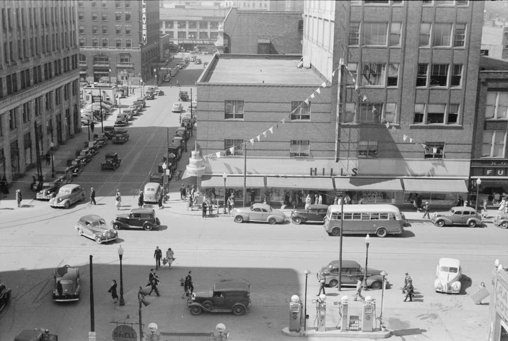 Businesses and Factories, pedestrian, Library of Congress, Cities and Towns, Portraits - Group, street lamps, Iowa History, Aerial Shots, downtown des moines, intersection, Main Streets & Town Squares, bus, downtown, ford model a, cars, Motorized Vehicles, banner, Iowa, gas pump, history of Iowa