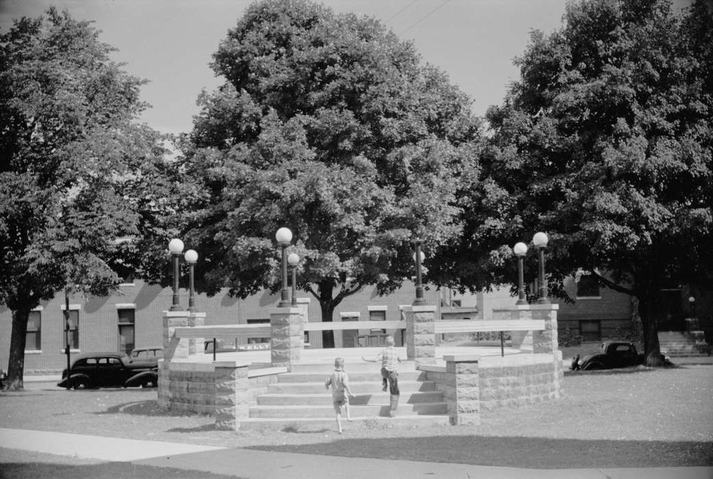 Main Streets & Town Squares, Library of Congress, town square, Cities and Towns, Iowa, Children, cars, Leisure, Portraits - Group, boys, pergola, lamppost, Families, Motorized Vehicles, history of Iowa, brick building, Iowa History, trees