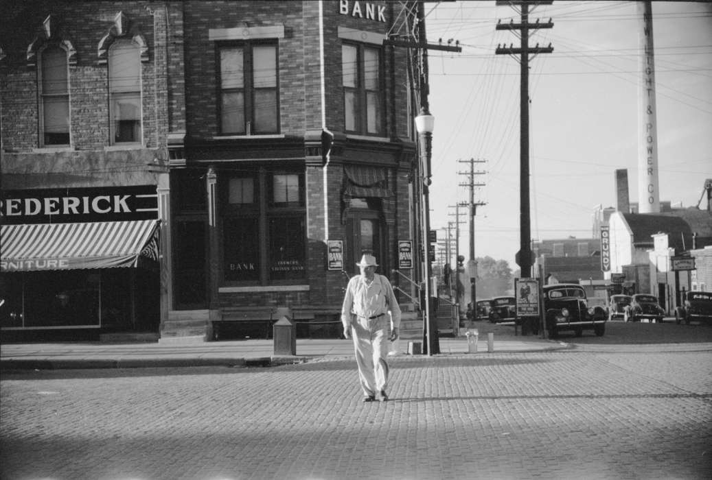 history of Iowa, brick building, Businesses and Factories, Library of Congress, Main Streets & Town Squares, power lines, man, Motorized Vehicles, sidewalk, Cities and Towns, lamppost, electric company, Iowa History, pedestrian, Iowa, cobblestone street, bank, electrical pole, Portraits - Individual, street corner