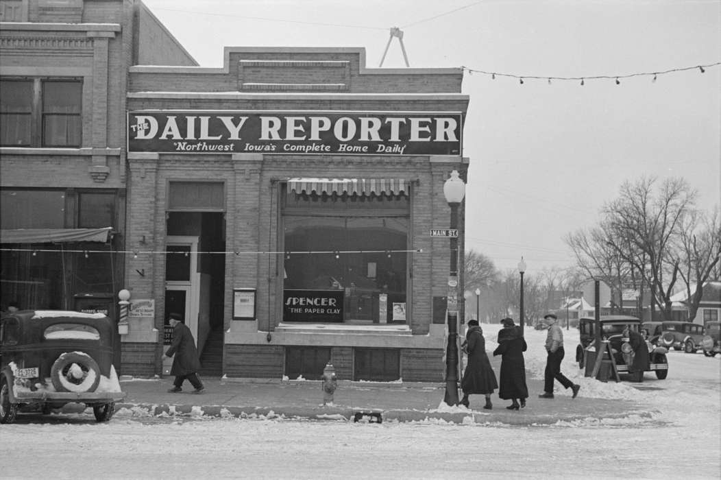 sidewalk, Cities and Towns, christmas lights, Motorized Vehicles, local newspaper company, Portraits - Group, lamppost, man, Winter, Iowa, Businesses and Factories, pedestrian, brick building, Library of Congress, fire hydrant, street corner, Iowa History, Main Streets & Town Squares, woman, history of Iowa, snow, car, Holidays