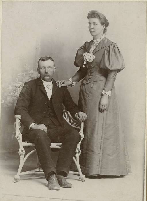 Olsson, Ann and Jons, couple, corsage, Iowa History, painted backdrop, Portraits - Group, sack coat, marriage, Iowa, chair, wicker chair, wing tip collar, Newton, IA, cabinet photo, Families, history of Iowa