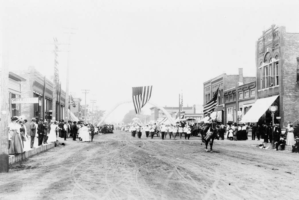 Fairs and Festivals, Businesses and Factories, american flag, Entertainment, marching band, main street, Cities and Towns, Civic Engagement, history of Iowa, parade, storefront, Main Streets & Town Squares, crowds, Library of Congress, Iowa History, Leisure, Children, Families, 4th of july, Animals, Holidays, dirt street, Iowa, Outdoor Recreation