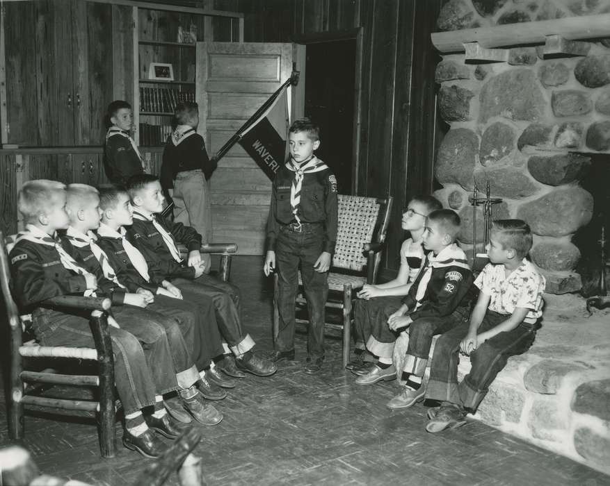 Waverly Public Library, banner, cub scout, fireplace, wicker chair, Iowa History, bolo tie, boy, neckerchief, history of Iowa, Leisure, bookshelf, book, Children, wood paneling, Iowa, uniform