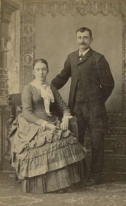 ruffles, Iowa, mustache, correct date needed, painted backdrop, bustle, Manchester, IA, vest, Iowa History, man, couple, Olsson, Ann and Jons, hairnet, lace collar, Portraits - Group, bow tie, frock coat, jabot, brooch, Families, woman, history of Iowa, carte de visite, necklace