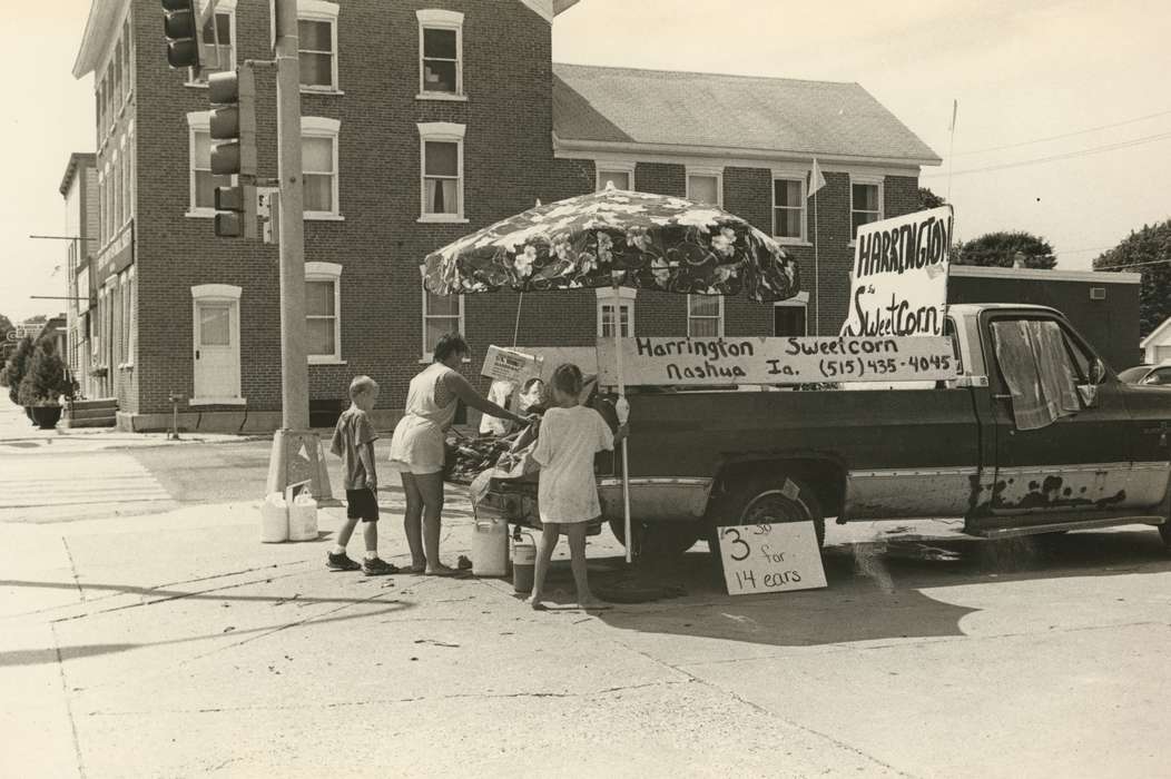 pickup truck, Motorized Vehicles, history of Iowa, Cities and Towns, Iowa, brick building, intersection, Main Streets & Town Squares, stoplight, Businesses and Factories, sidewalk, umbrella, Children, sweet corn sale, Portraits - Group, Waverly Public Library, sweet corn, Iowa History, Labor and Occupations, Families, kids